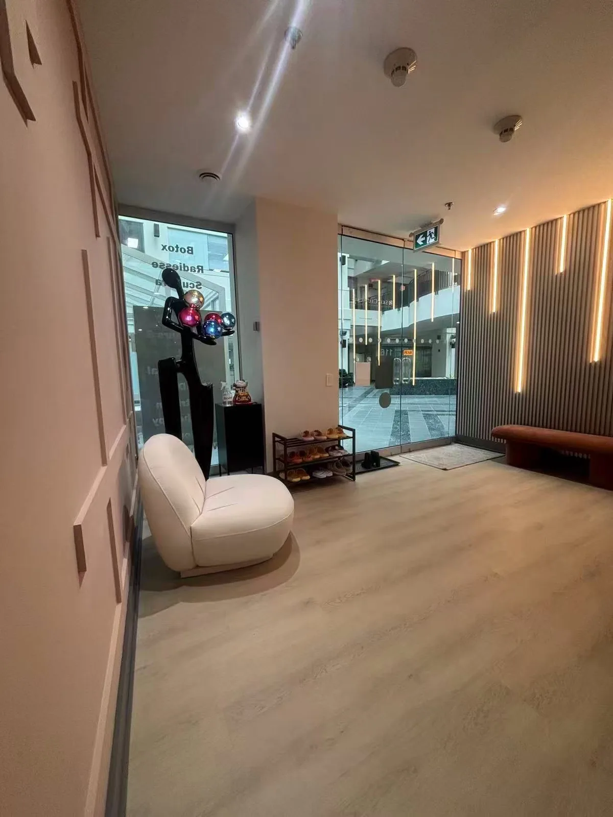The reception lobby at Artistry Clinic, with a fluted timber wall, warm linear lighting, and a single sculptural chair.