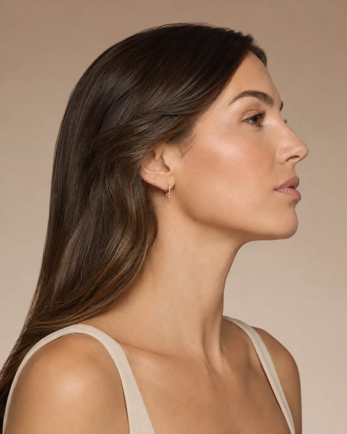 A side profile of a woman, photographed against a warm neutral background at Artistry Clinic.